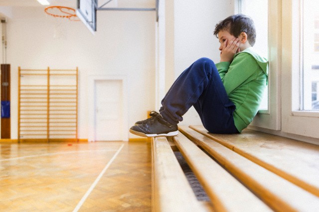 22 Mar 2013 --- Boy sitting alone on bench in school hall --- Image by © Annie Engel/Corbis